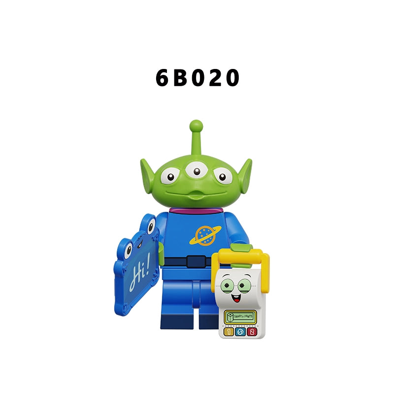 A toy figure resembling a green three-eyed alien in a blue space suit, holding a blue book and standing next to a small white and yellow smiling character, on a plain white background with the text '6B020' above.